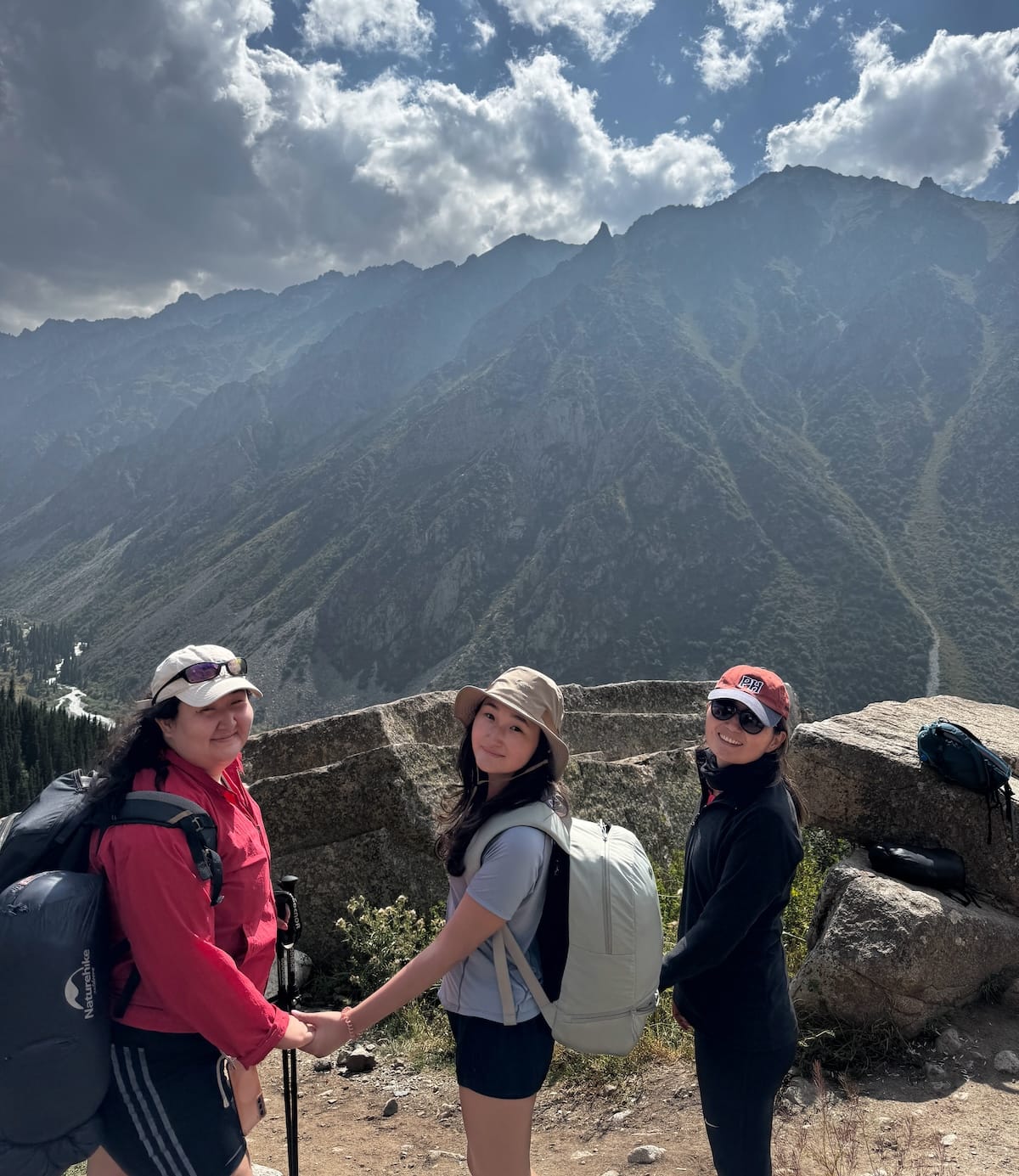three sisters in hiking gear standing in front of a tall mountain