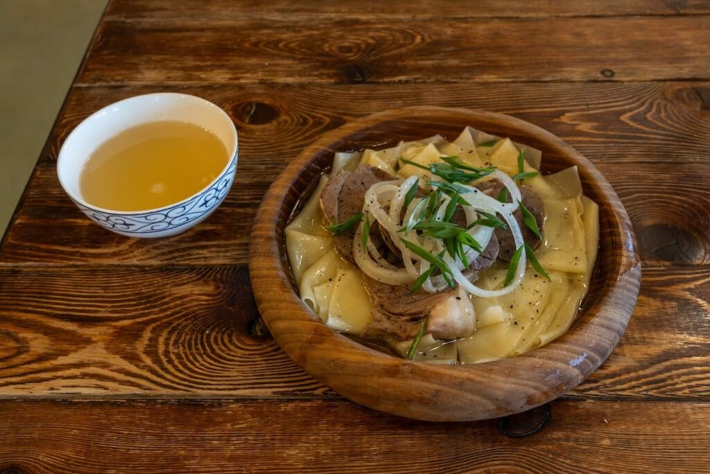 A plate of beshbarmak and a side of sorpa on a table
