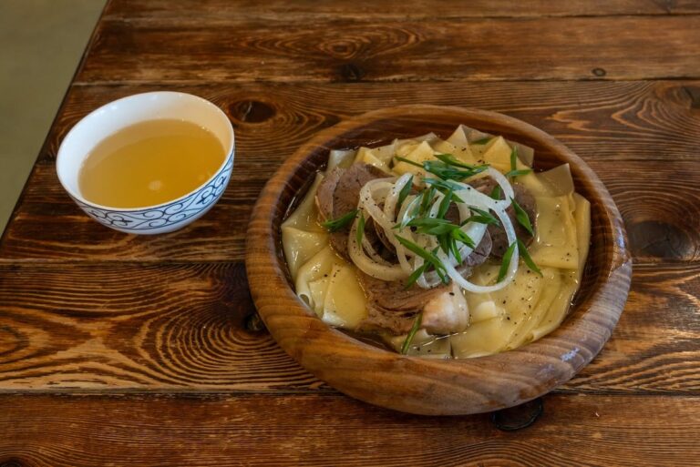 A plate of beshbarmak and a side of sorpa on a table