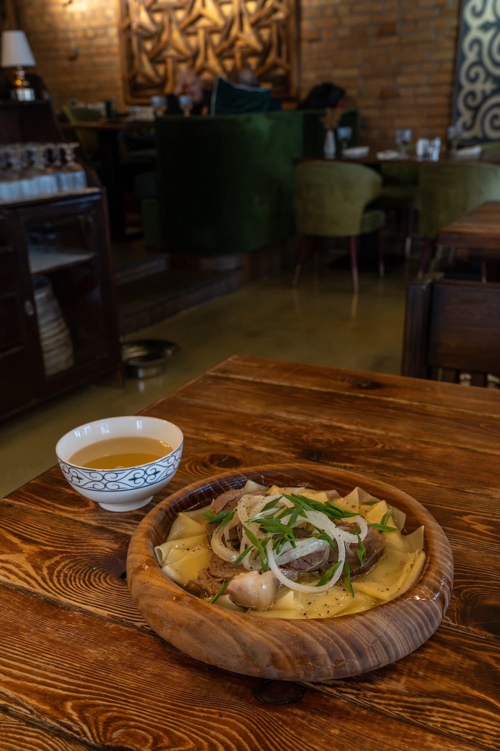A plate of beshbarmak and sorpa on a wooden table