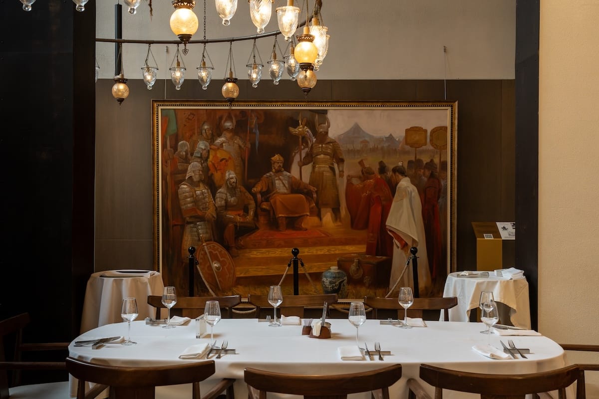 Inside a restaurant with a large table with a tablecloth and a painting behind it