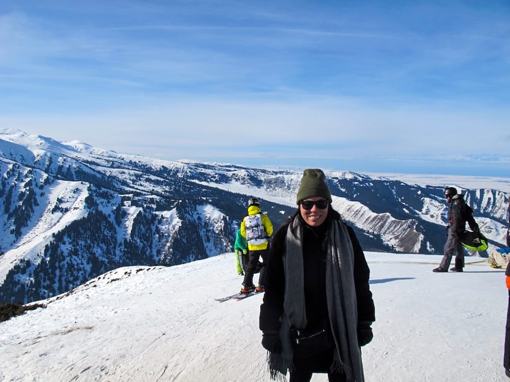 a woman standing on a mountain where people are skiing