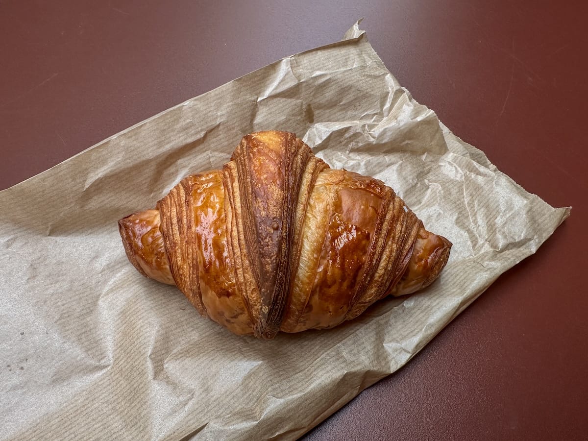 a croissant on a maroon table with a to-go bag