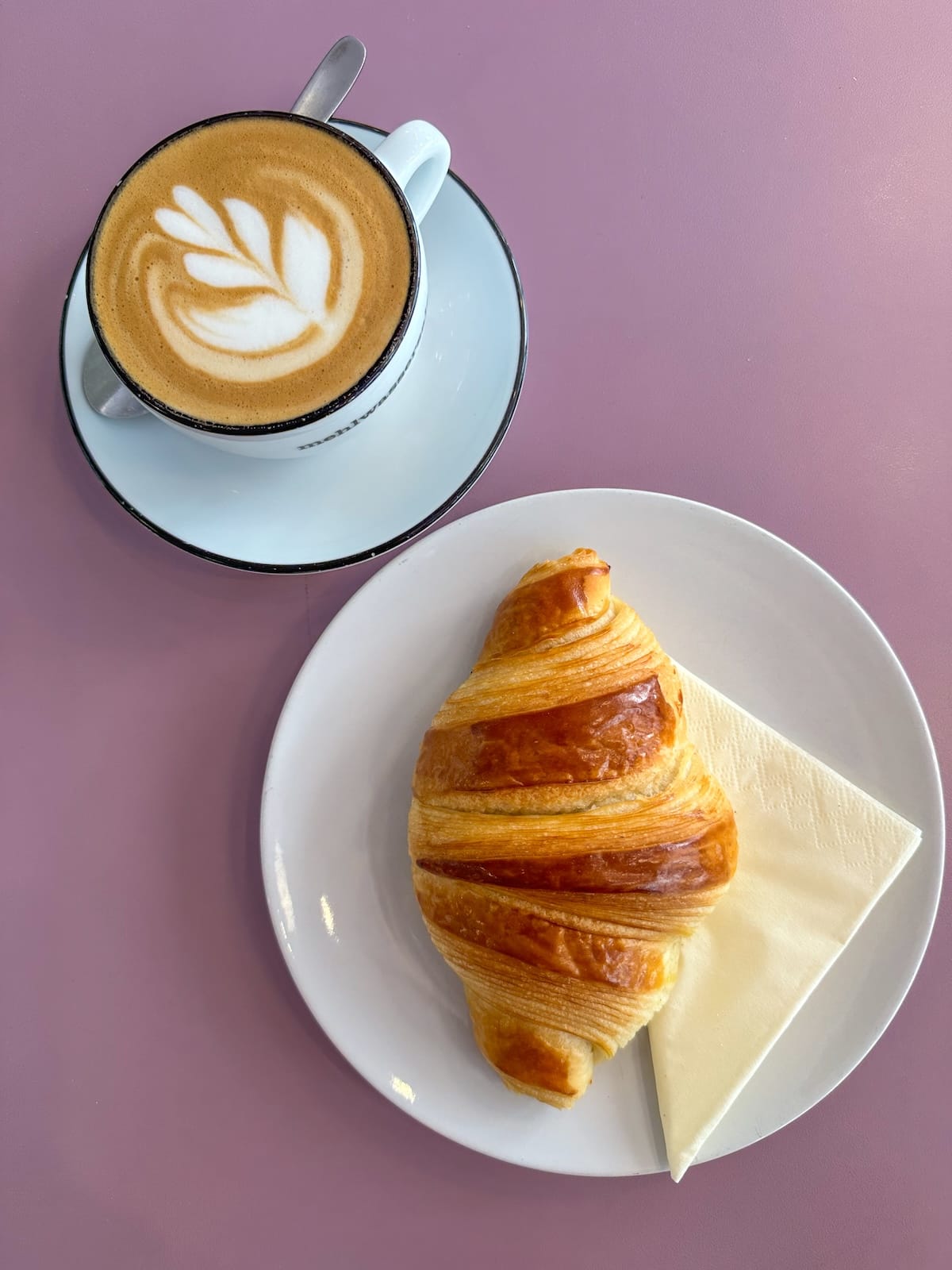 a sourdough croissant and coffee on a pink table