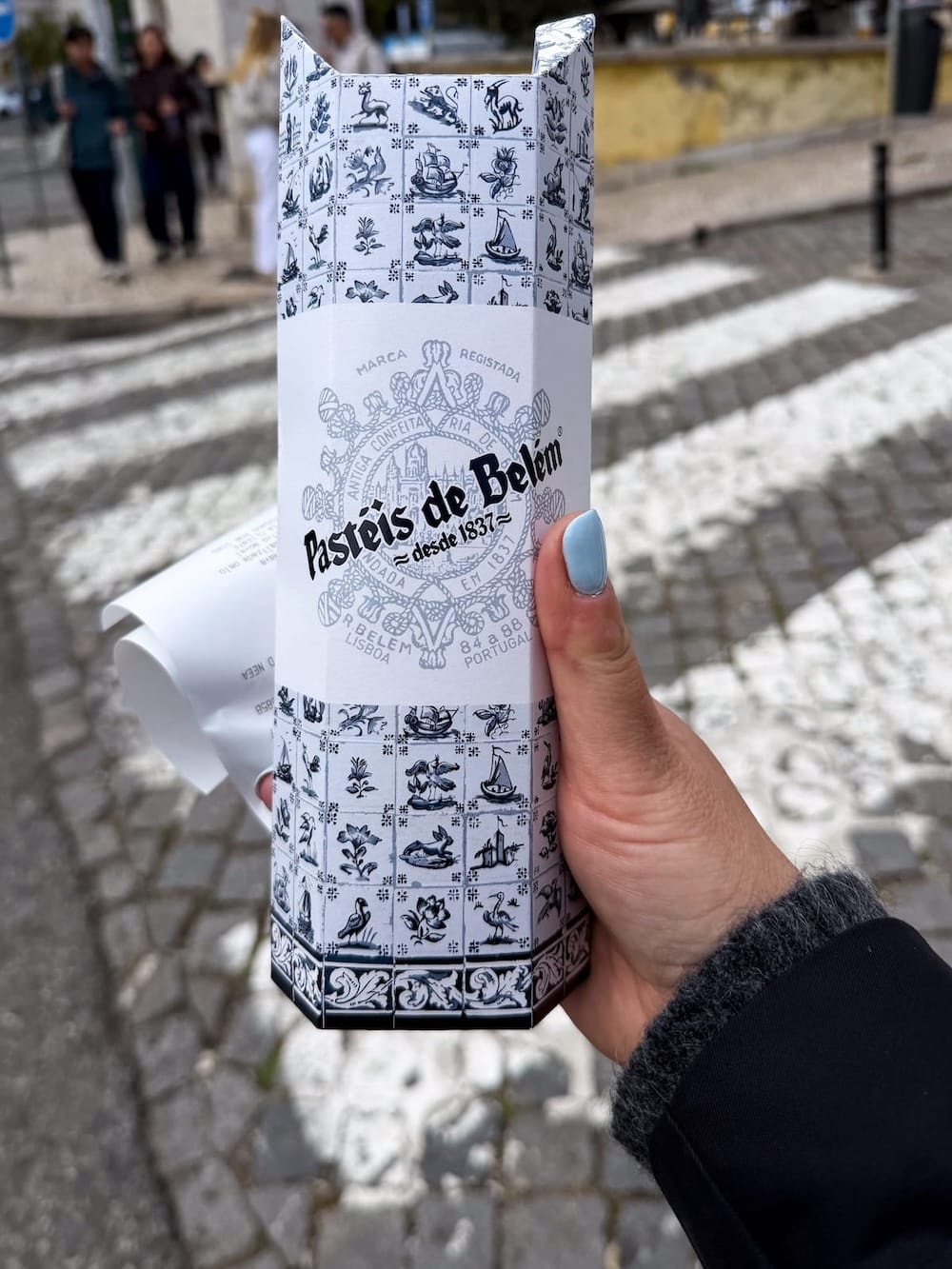 a box of pastel de natas outside a monastery in a woman's hand