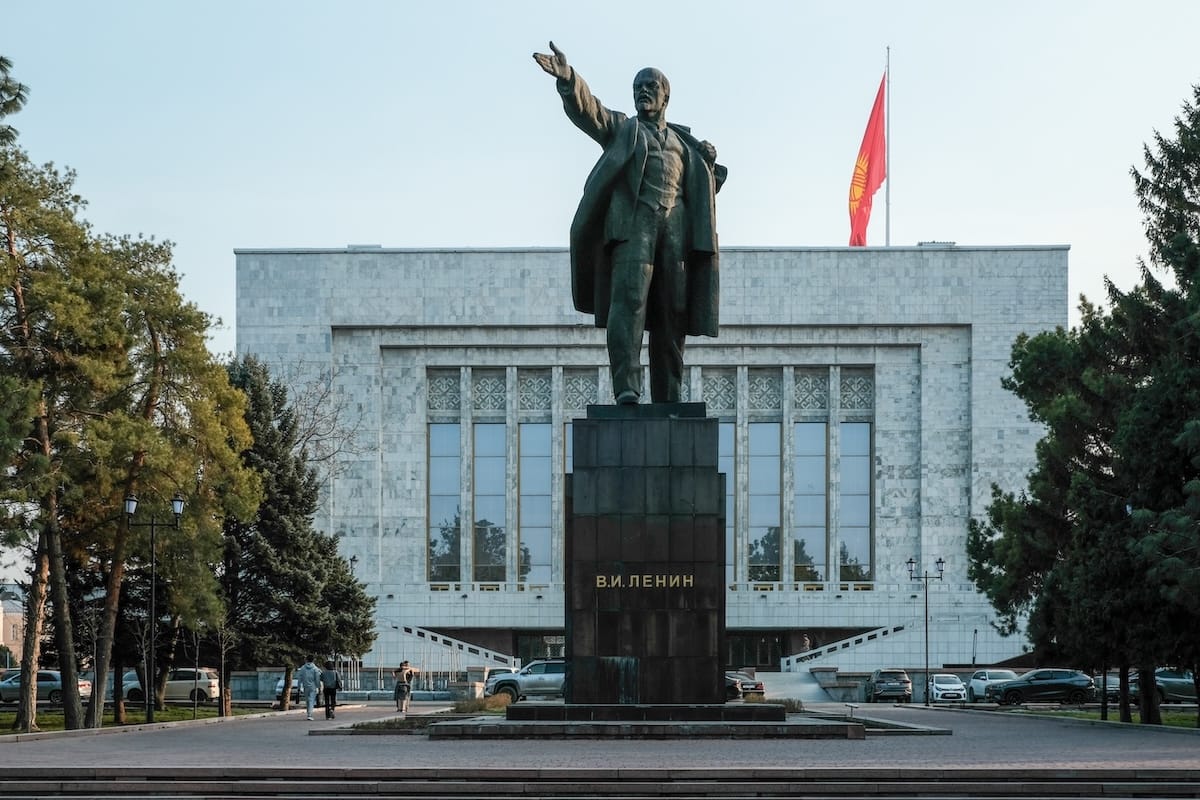 a statue of lenin with a kyrgyzstan flag behind him in front of a museum