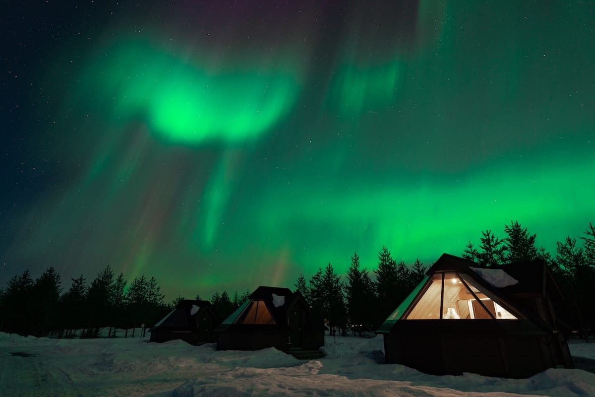 a glass igloo under the green northern lights