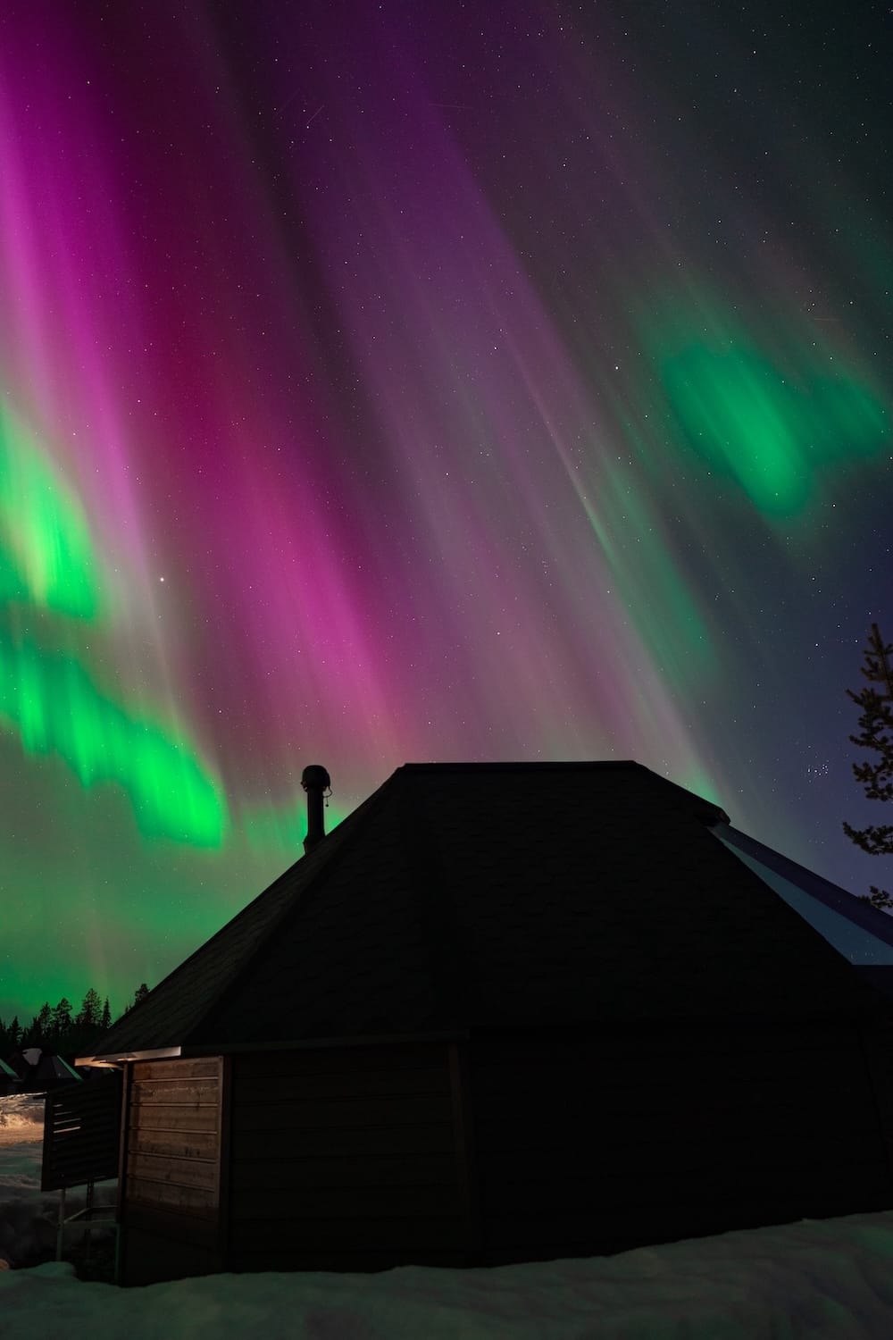 A glass igloo under pink and green northern lights