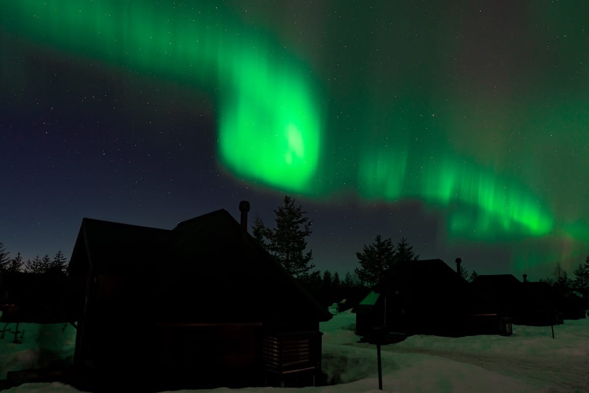 A glass igloo with a light off under the aurora
