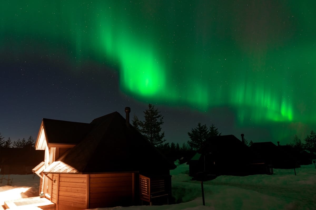 A glass igloo with a light on under the aurora