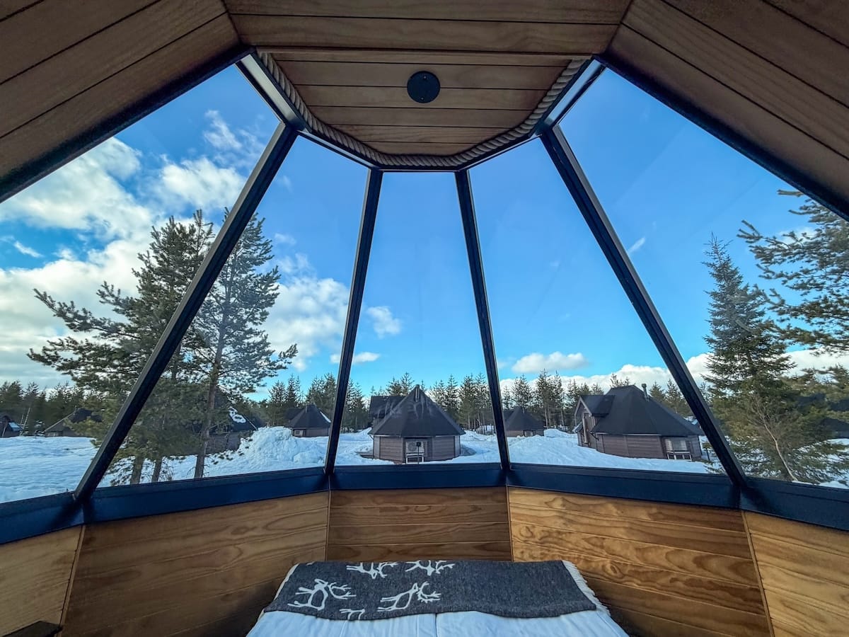 a bed in a circular glass igloo cabin with trees and snow on the outside
