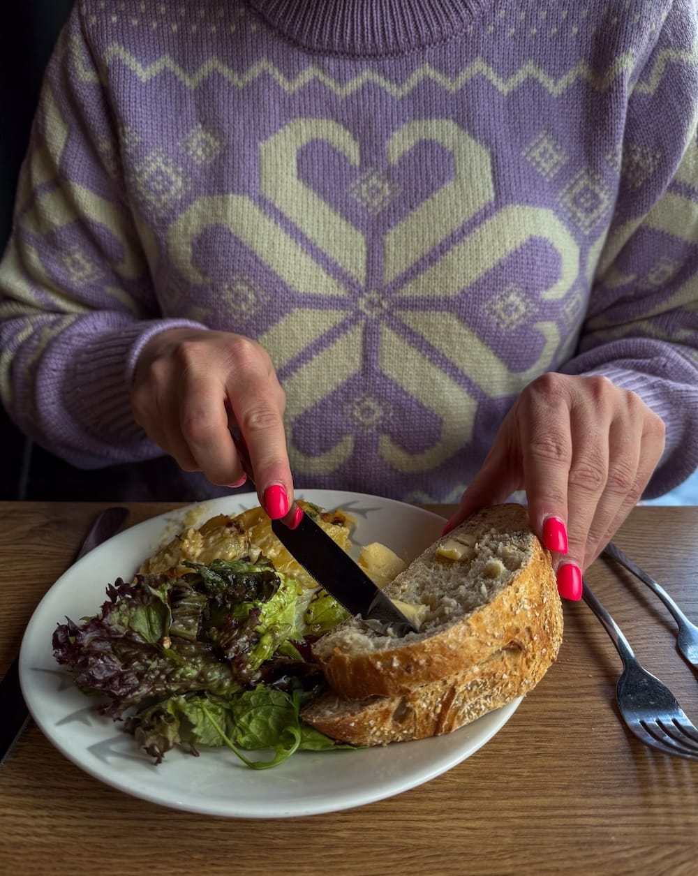 a woman in a purple sweater buttering bread on a plate