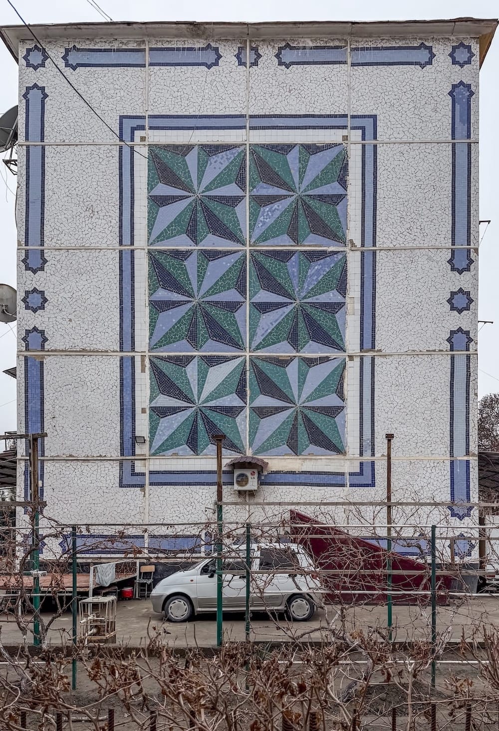 a blue and teal mosaic on a building with a car in front of it