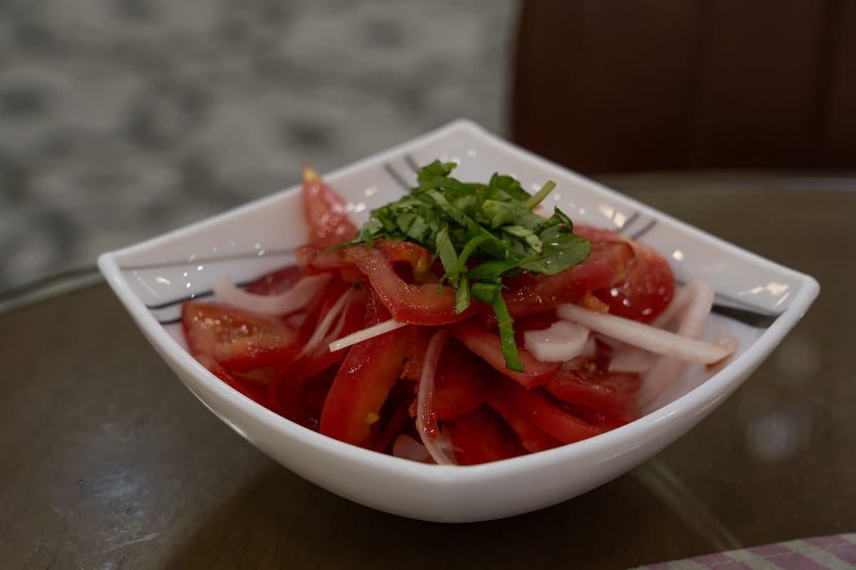 a bowl with sliced tomatoes, onions, and herbs on top of it