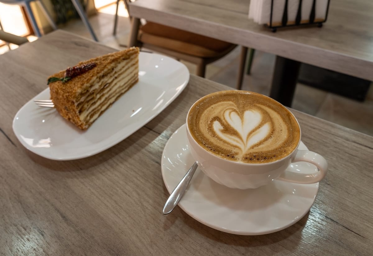 a flat white with latte art and a medovic honey cake on a table