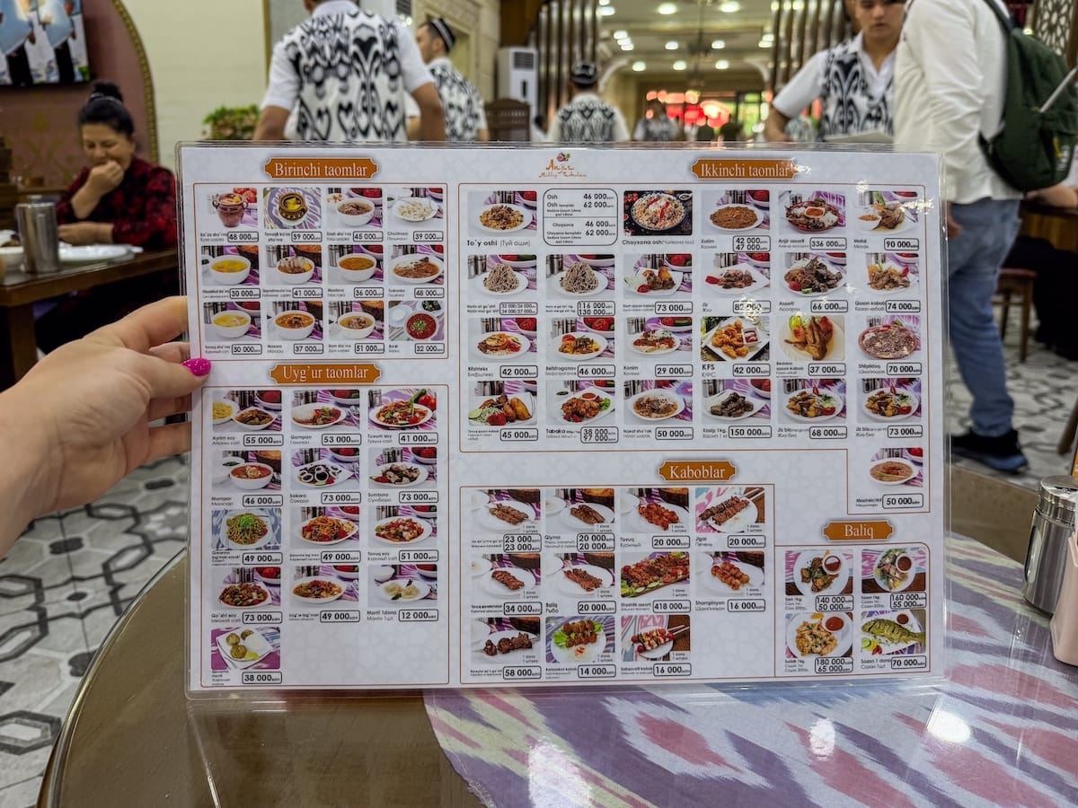a laminated white menu with a ton of photos of dishes on it - all in Uzbek