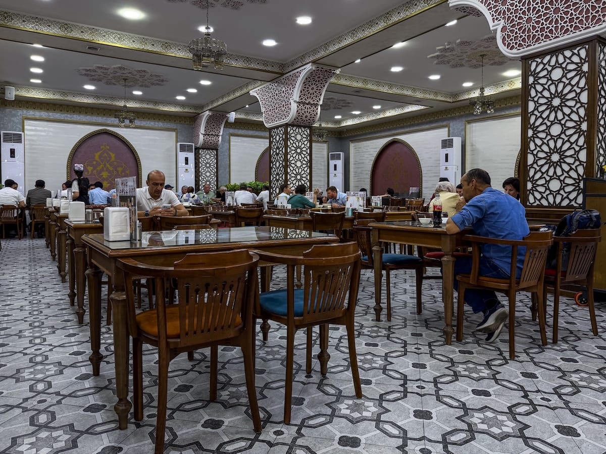 the interior of a plov restaurant in tashkent - many wooden tables inside with a tiled floor