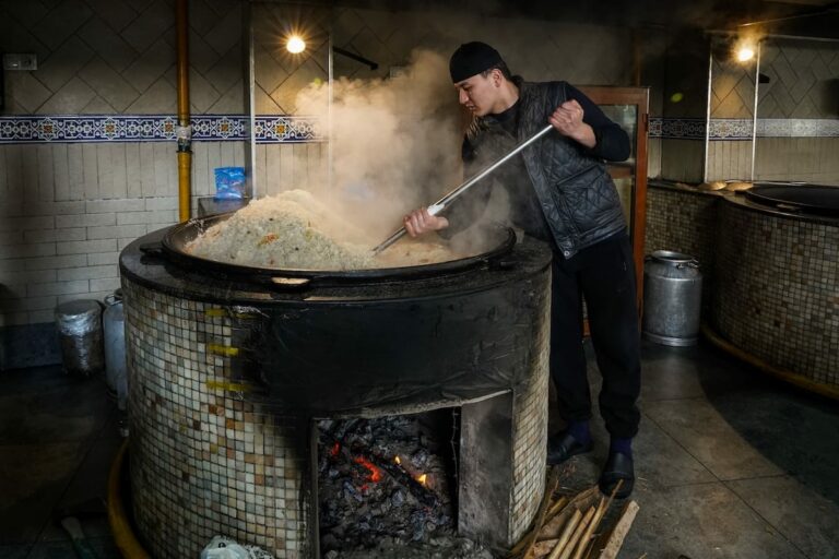 Where to eat plov in Tashkent a man standing over a huge kazan cooking plov in uzbekistan