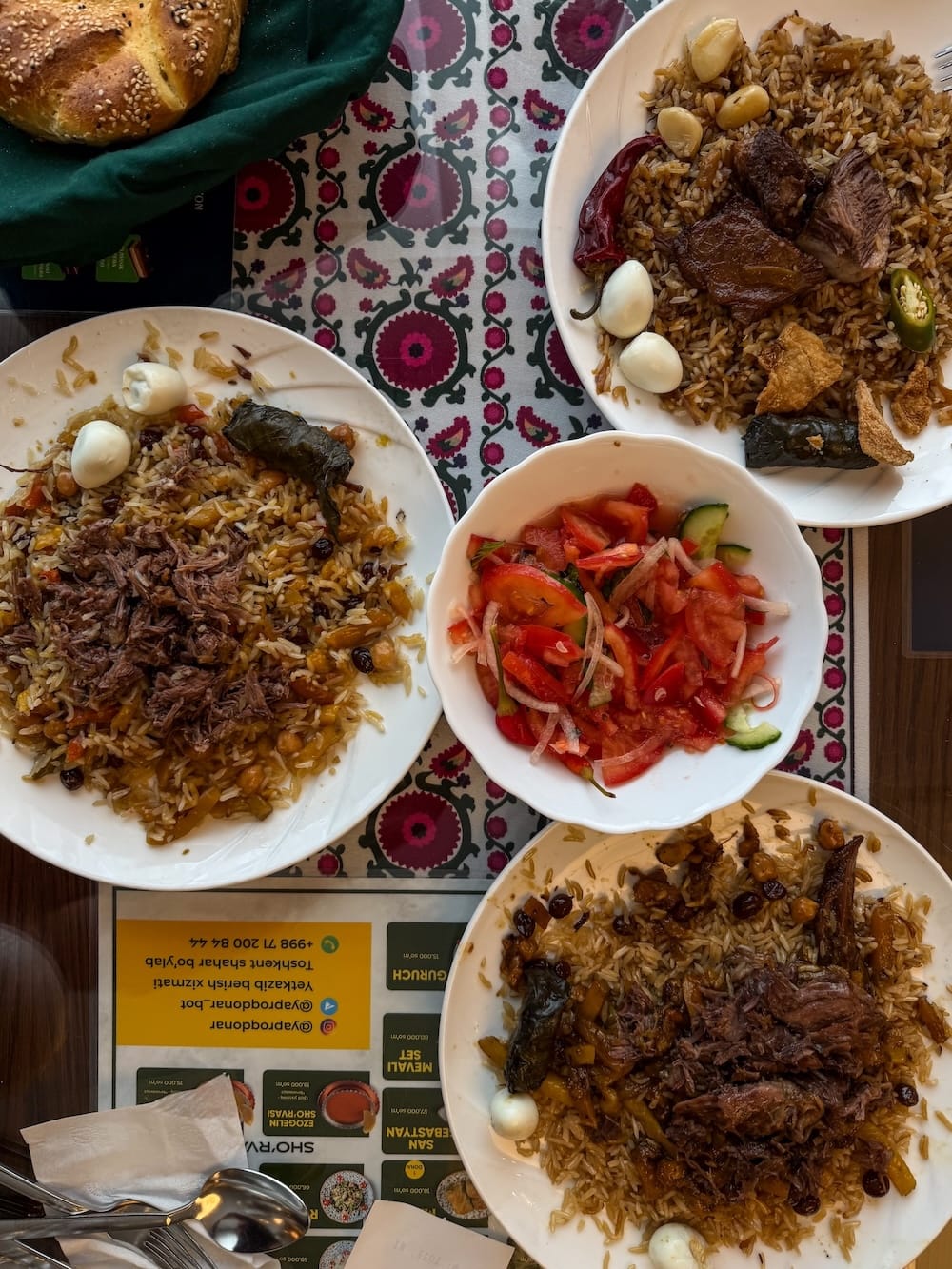 three plates of plov on a table with a bowl of tomatoes in the middle