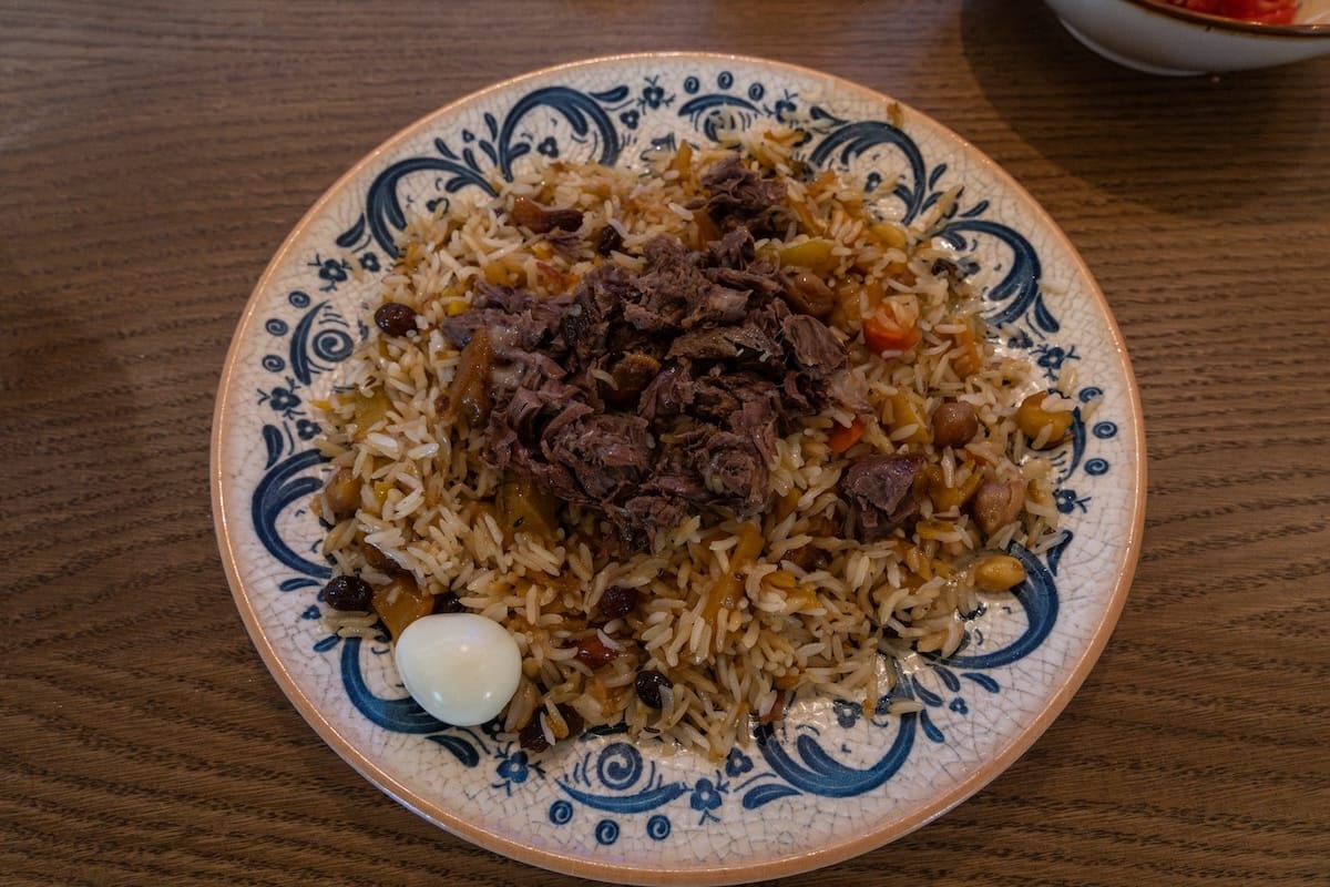 a plate of plov on a table with meat on top and a single quail egg