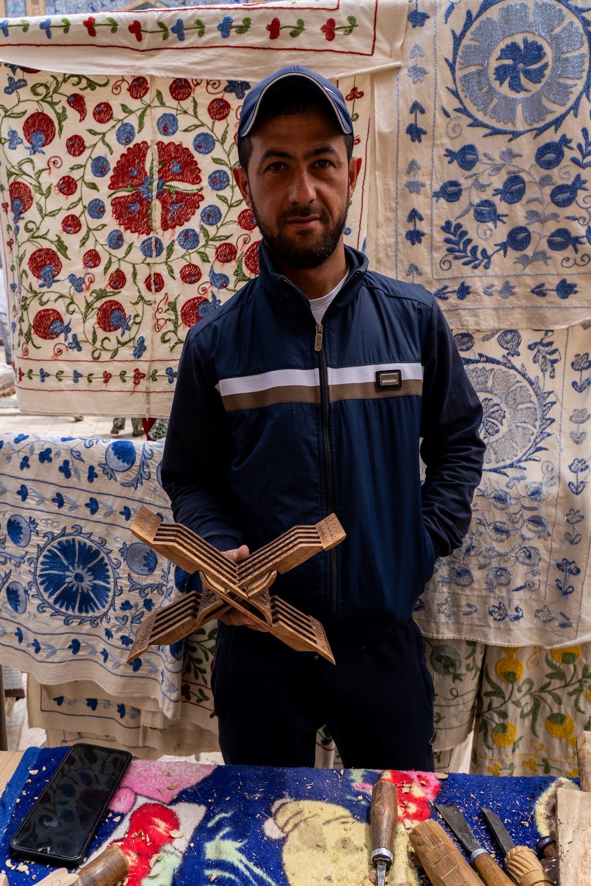 a photo of a man in a tracksuit holding up a wood carving he made in uzbekistan