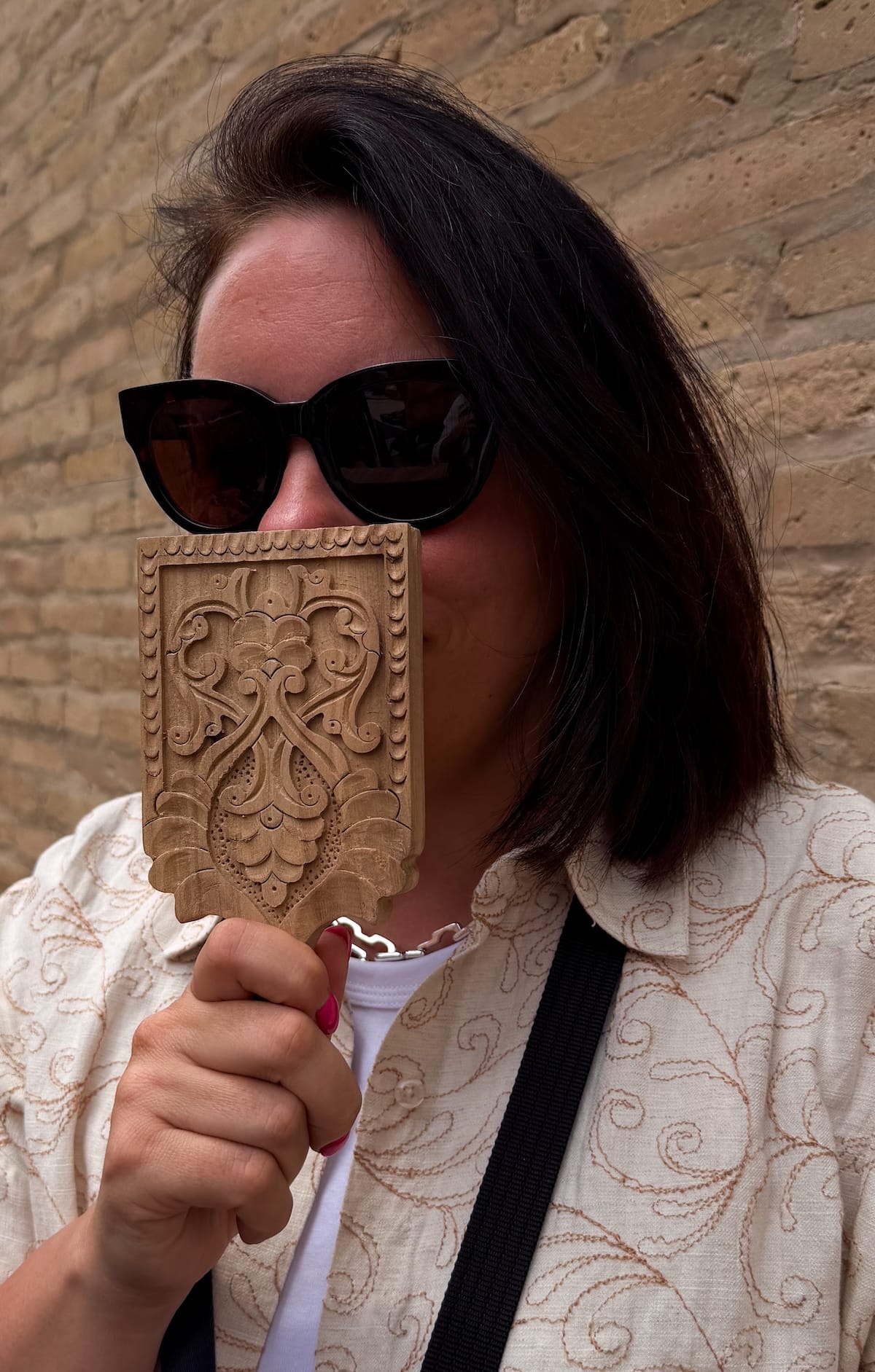 a woman holding up a wooden carving in front of her face to show scale