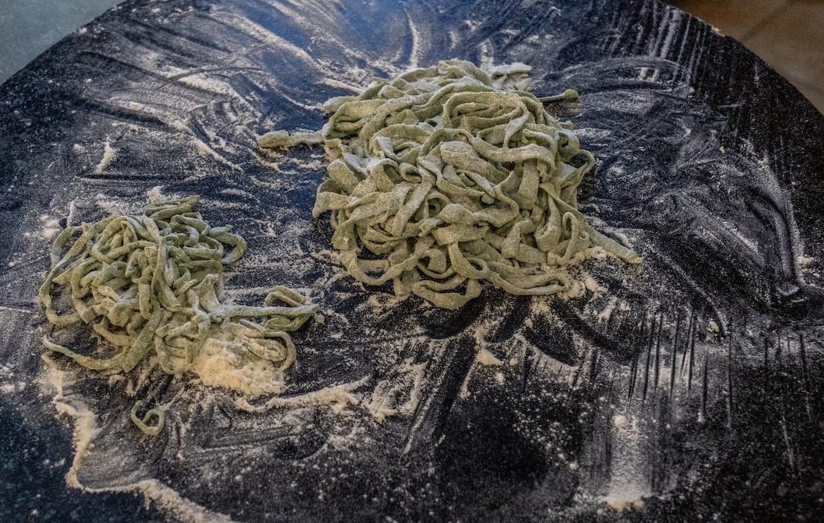 a table with green pasta being made on it with flour
