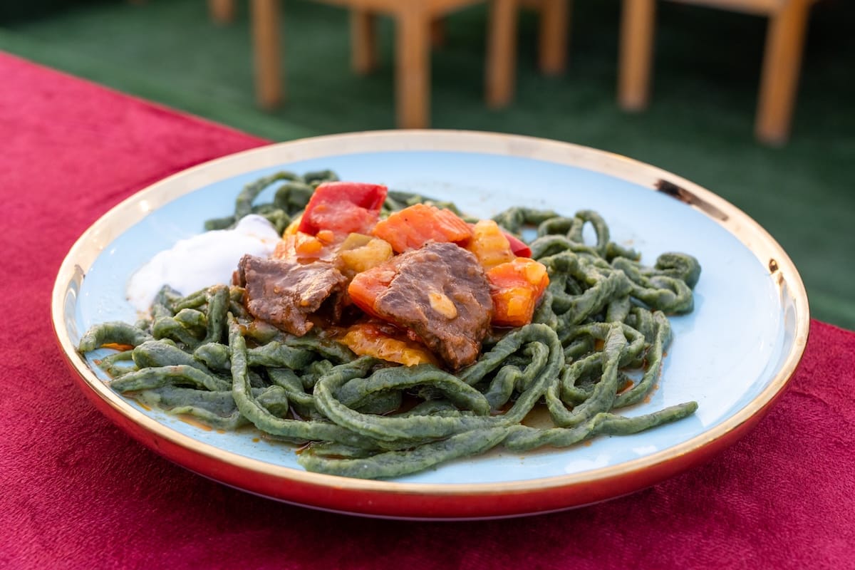 a plate of green dill noodles, yogurt, meat, and potatoes on a table