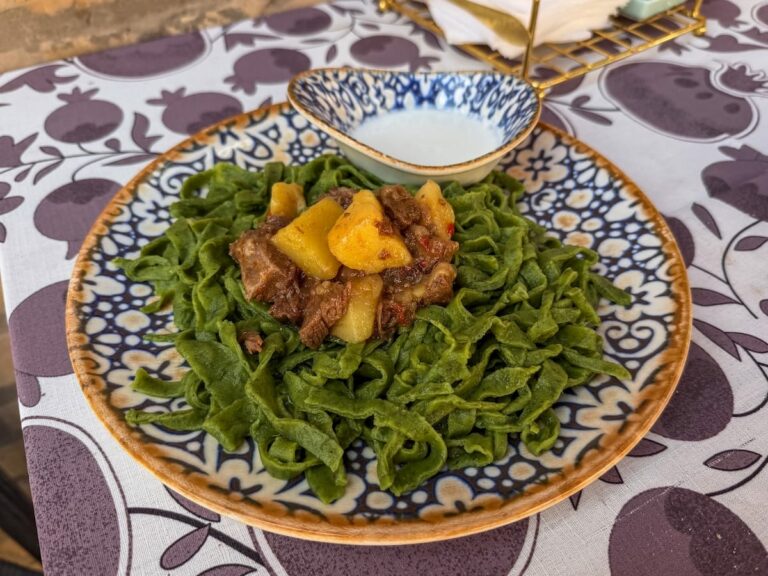 a plate of shivit osh on a table in a restaurant - it is a green noodle dish with meat and potatoes and yogurt sauce