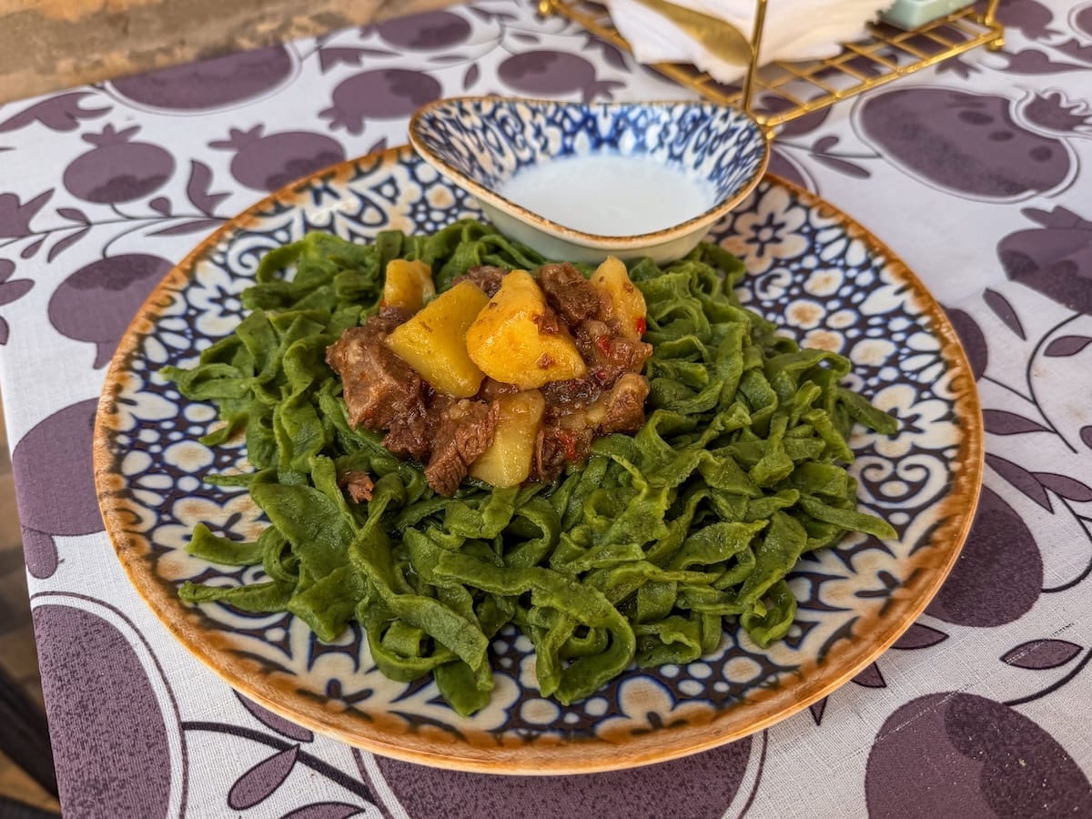 a plate of shivit osh on a table in a restaurant - it is a green noodle dish with meat and potatoes and yogurt sauce