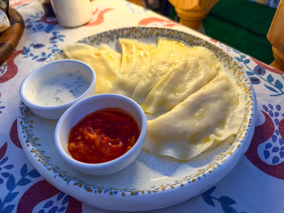 A plate of egg filled dumplings with a white creamy sauce and a red sauce on a table