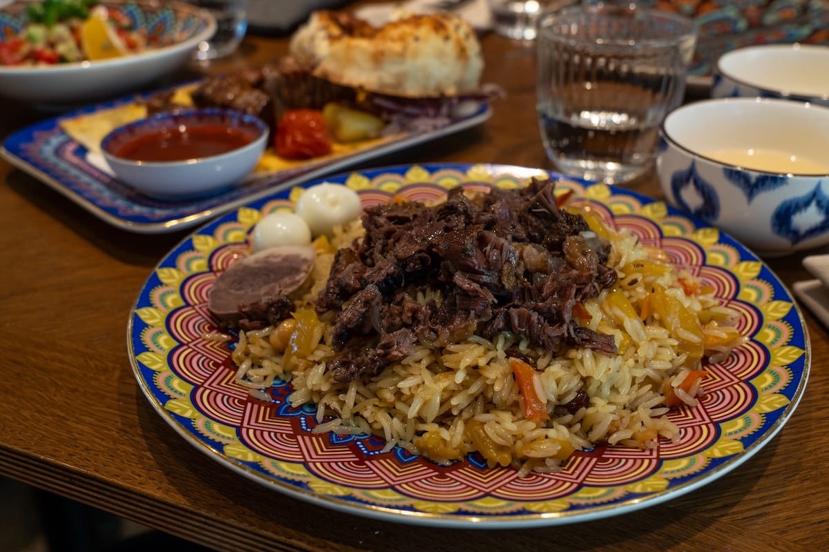 a plate of plov on a table - the plov has meat, 2 quail eggs, and a horse sausage in it