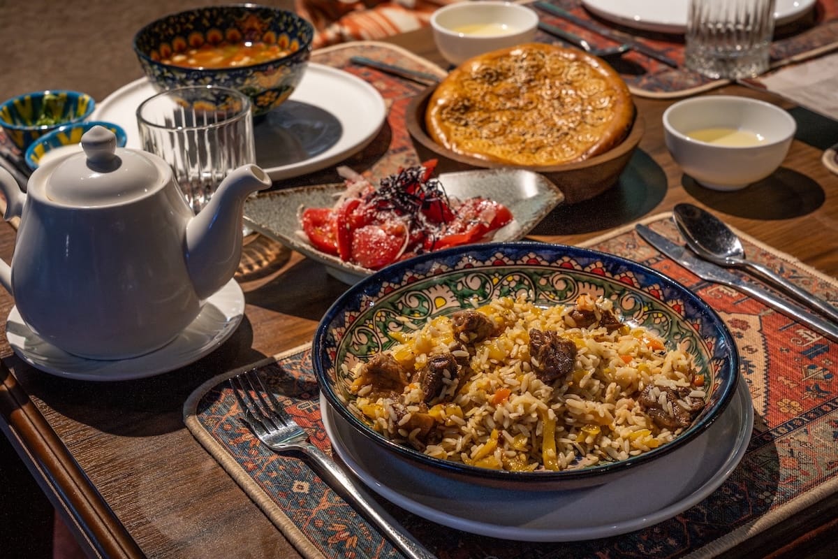 a plate of uzbek plov on a table with other regional foods from fergana valley behind it