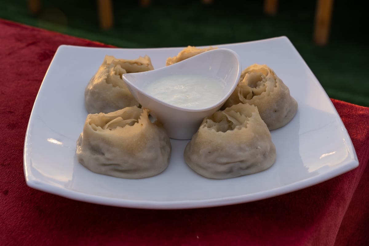 dumplings on a plate on a red tablecloth with sour cream in middle