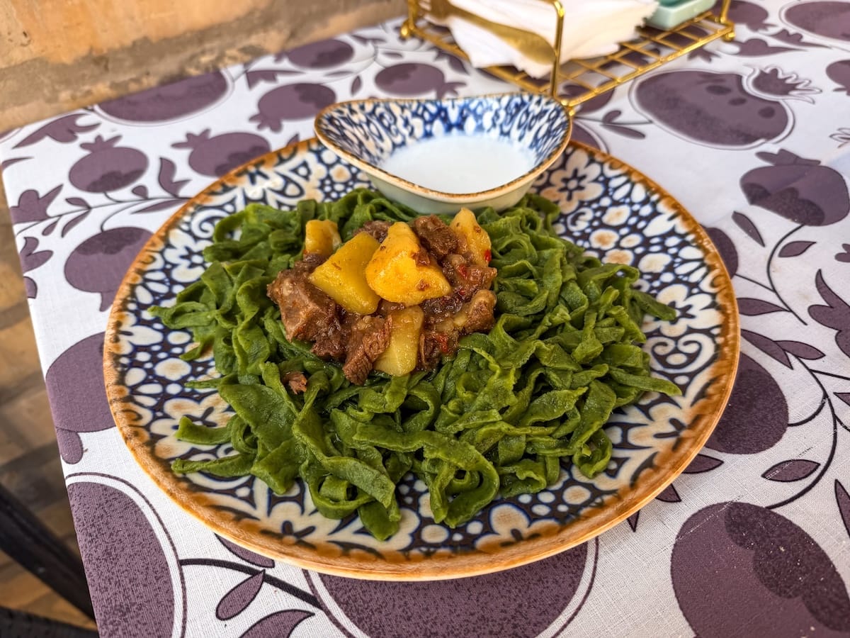 a plate of green dill noodles, meat, yoghurt sauce, and more on a table