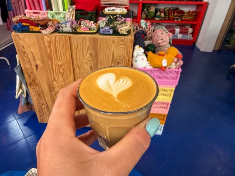 a woman holding a flat white in a glass in her hand in a cafe Best coffee shops and cafes in Ciutadella, Menorca (Bubu's Corner)
