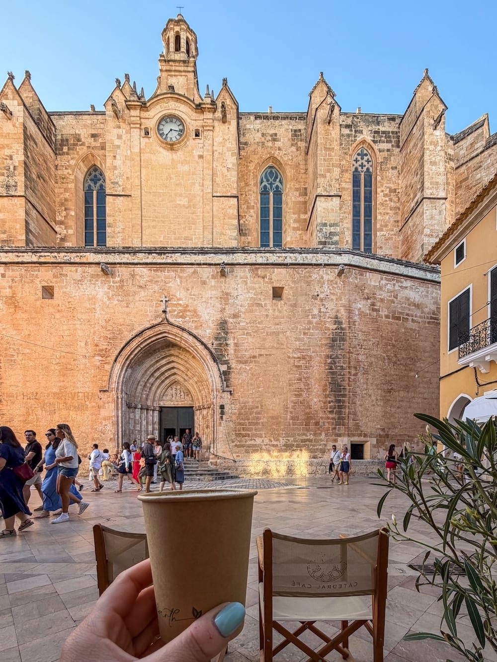 A cathedral in an old town in Spain with a woman holding a coffee in front of it