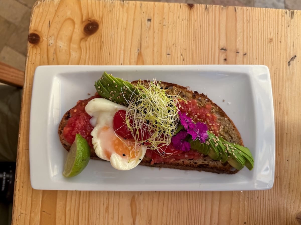 a piece of bread with tomatoes, poached egg, avocado, and sprouts on top of it