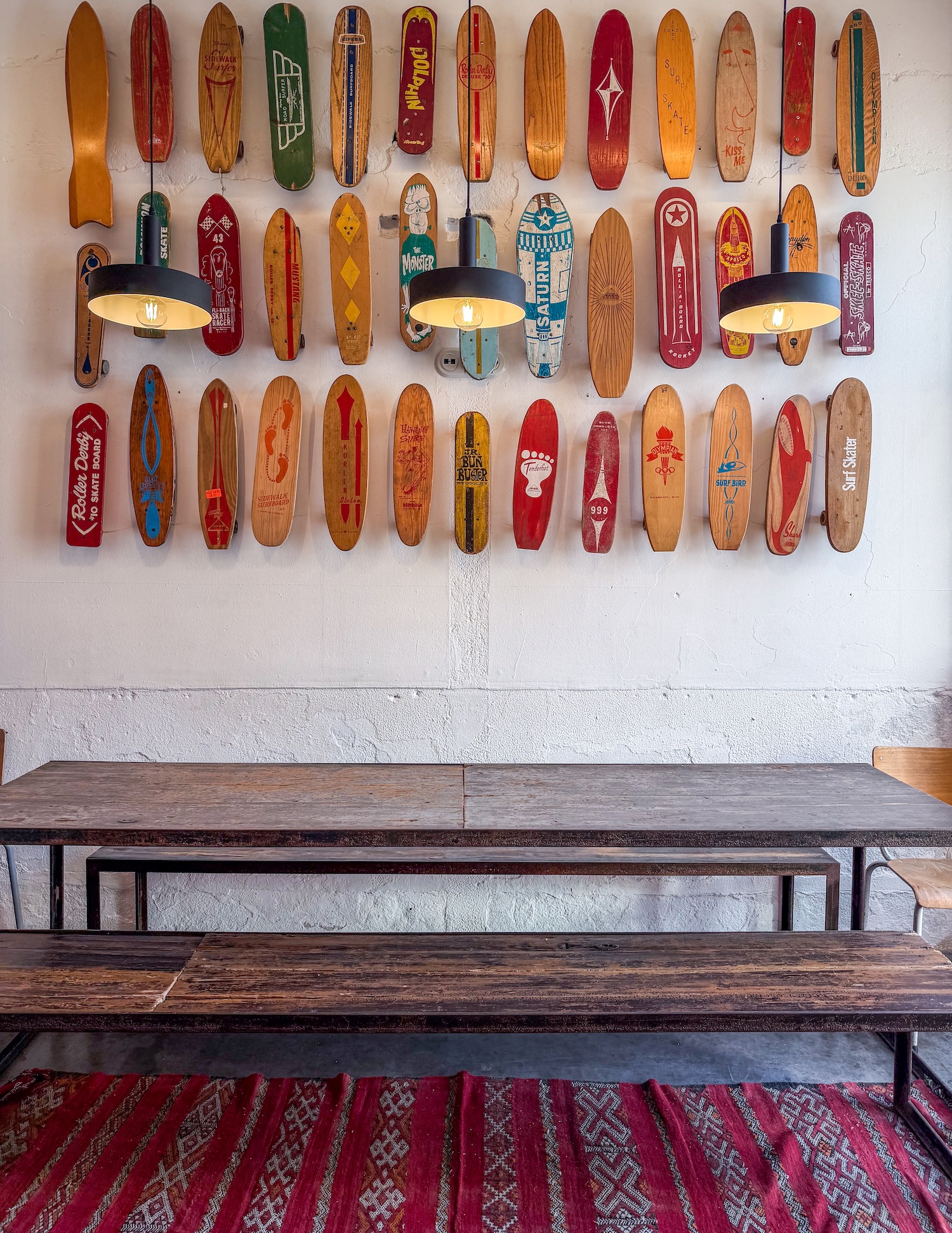 a table in a hip restaurant with a bunch of skateboard and mini surfboards on the wall as decor