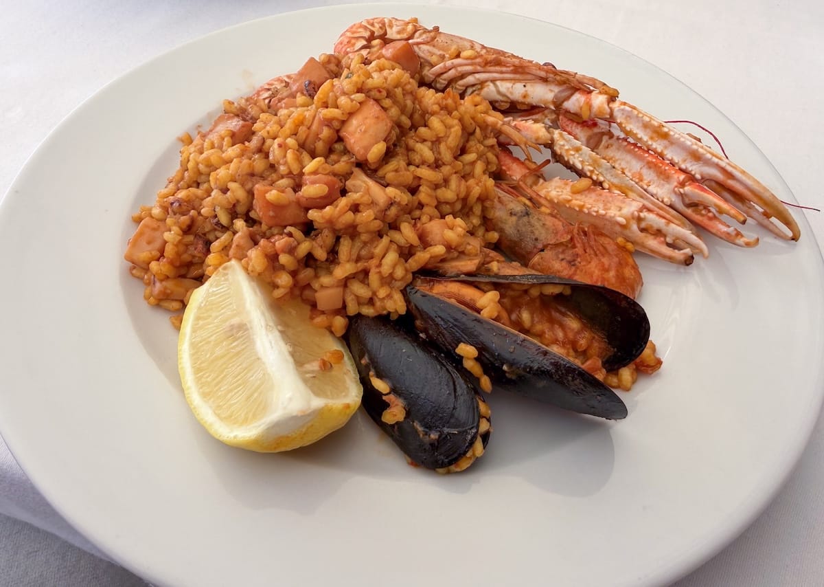a plate of paella with two mussels and a lemon on a plate