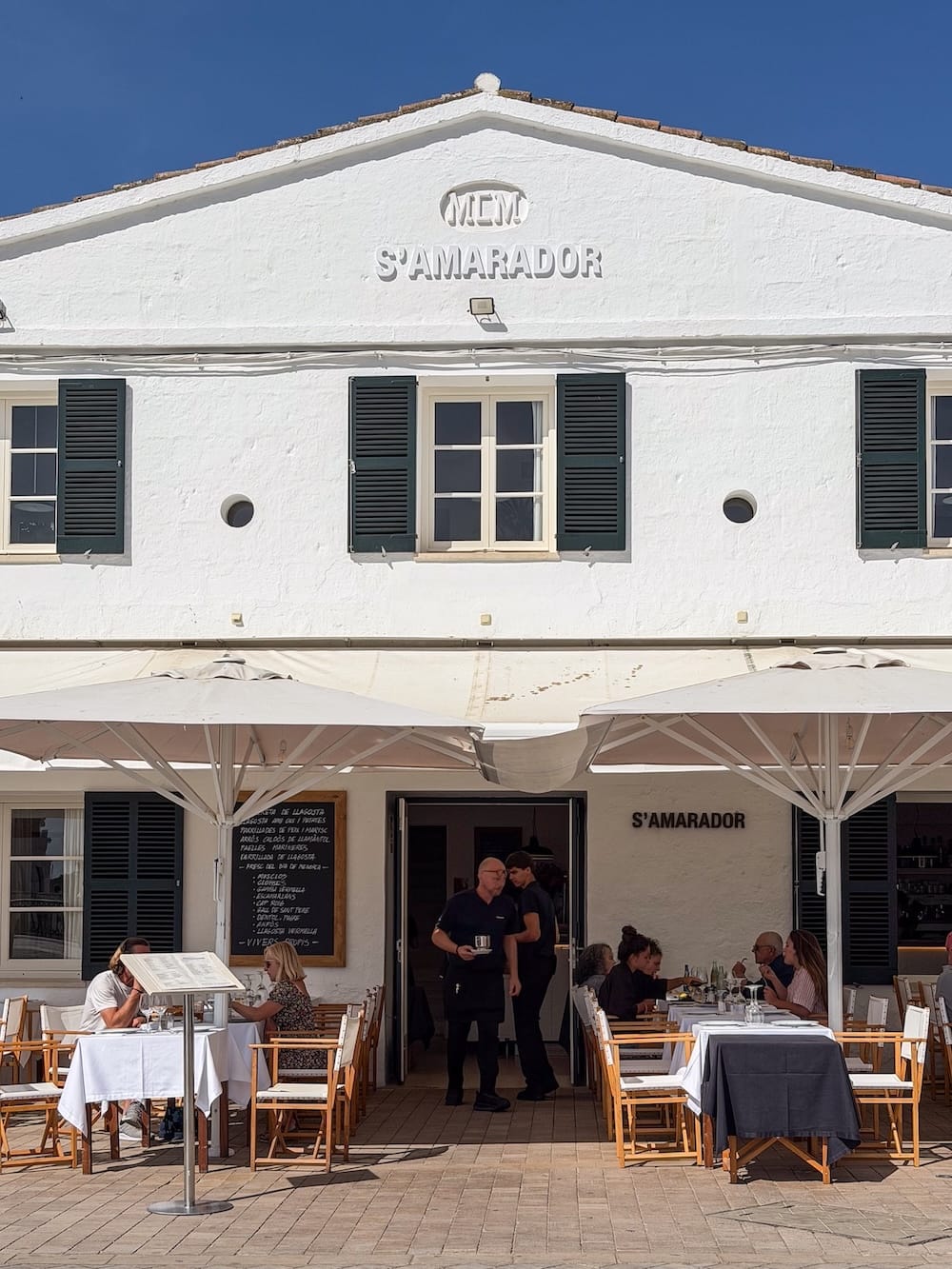 a white restaurant with a terrace and people sitting outside