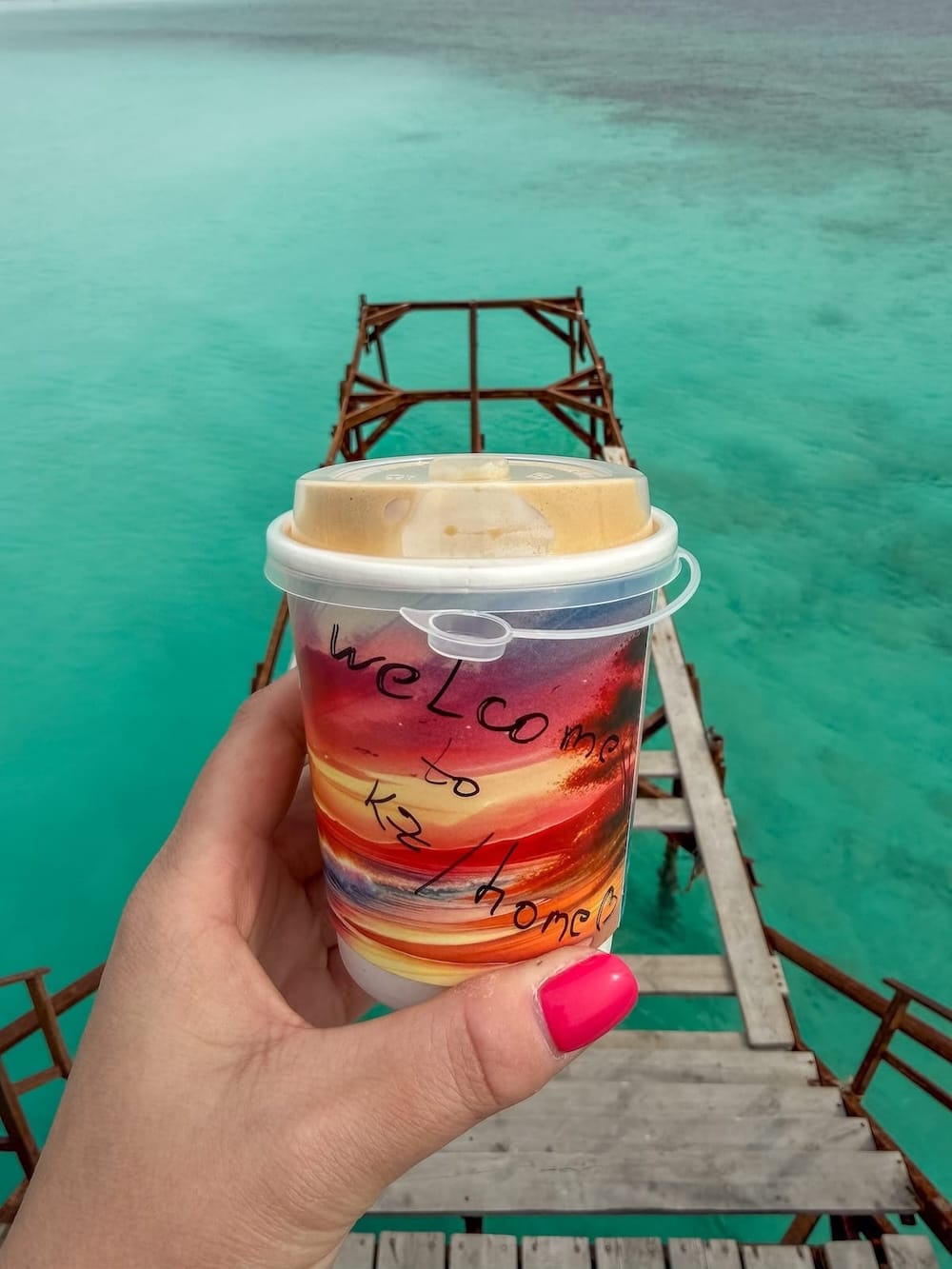 a woman's hand with a colorful coffee cup in it by the sea