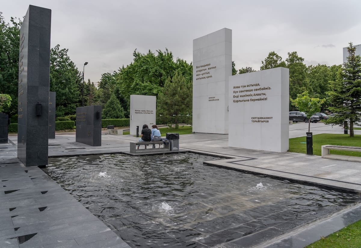 A memorial in Almaty with two people sitting by it.