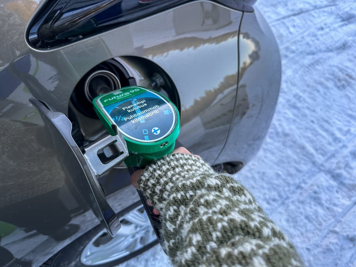 a woman in a sweater filling up gas in a rental car