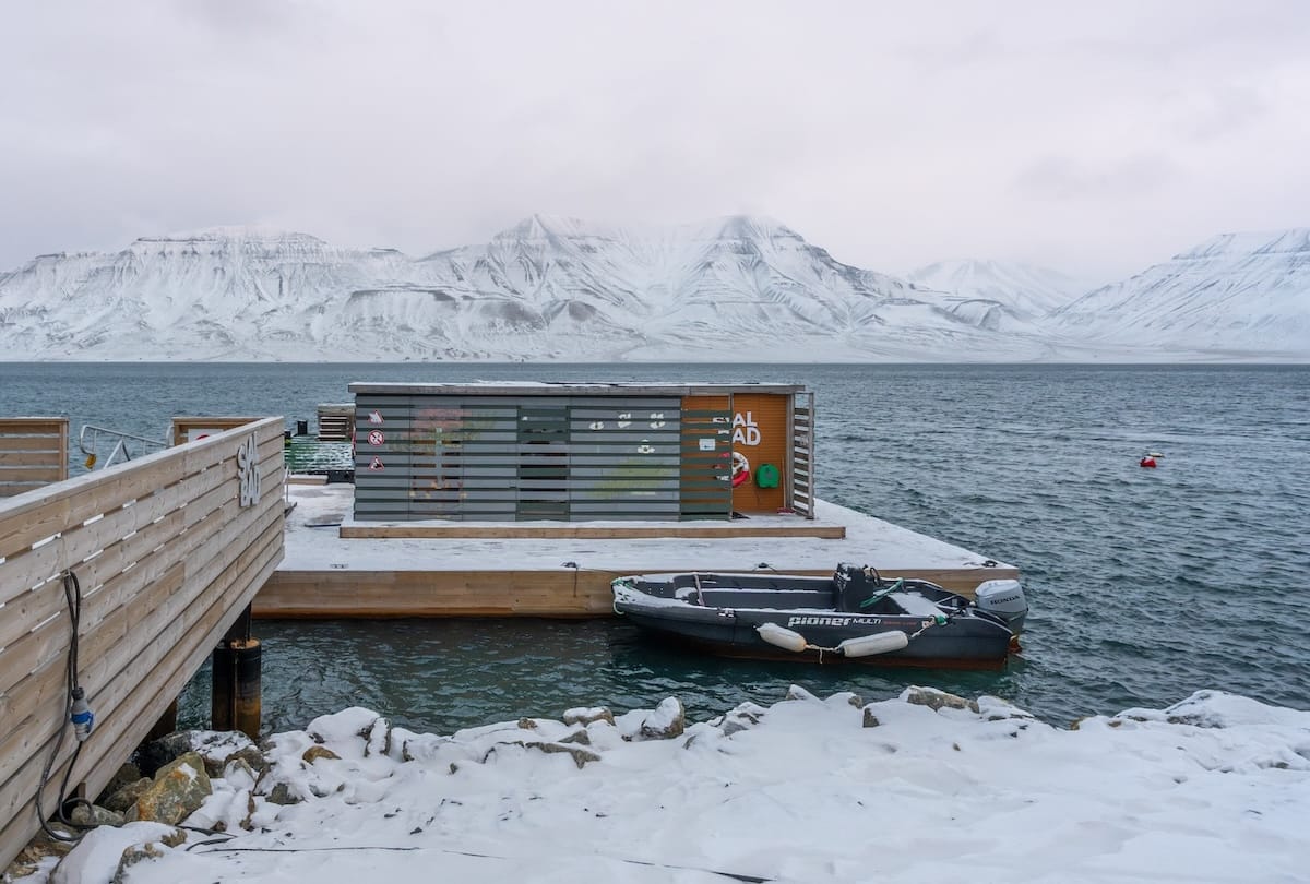 a sauna on a fjord with snow on mountains behind it