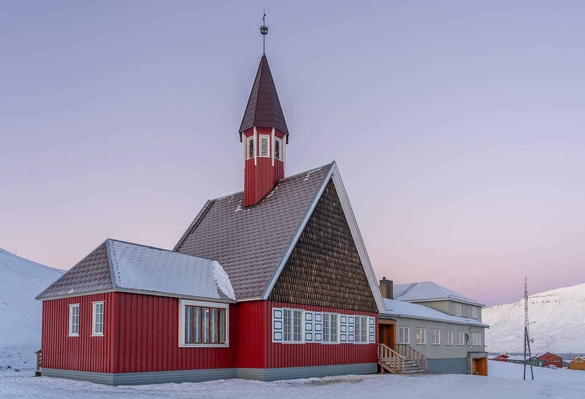 a red church made of wood in svalbard under a purple sky