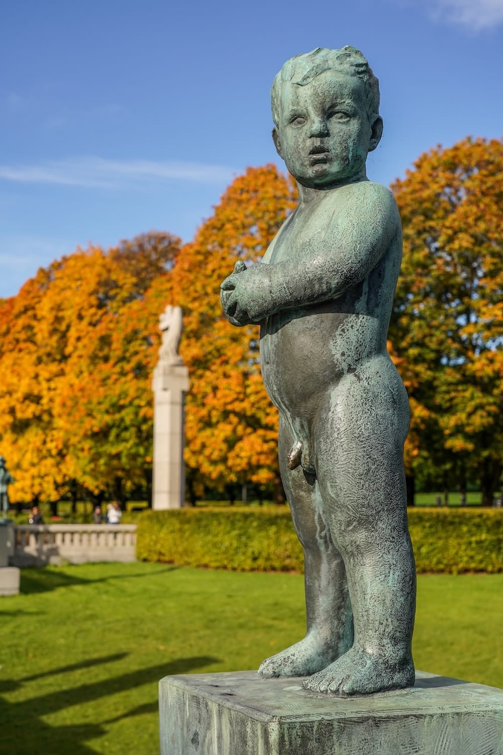 a famous statue in a norwegian park of a baby with fall colors behind it