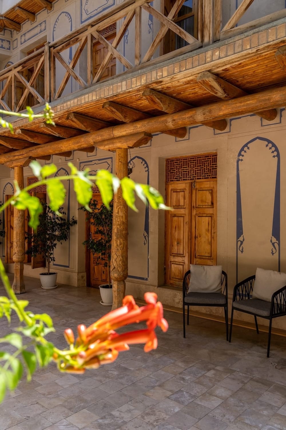 Traditional wooden balcony and painted archways at Ayvan Restaurant's courtyard in Bukhara, Uzbekistan