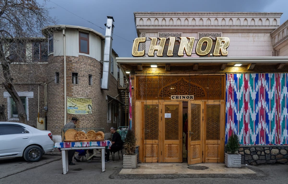 Exterior of Chinor restaurant with illuminated sign and fresh bread stand in Bukhara, Uzbekistan