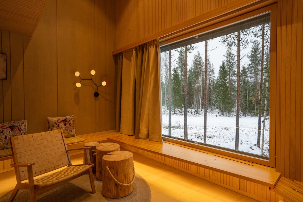 a warm toned apartment with a large window facing snowy forest